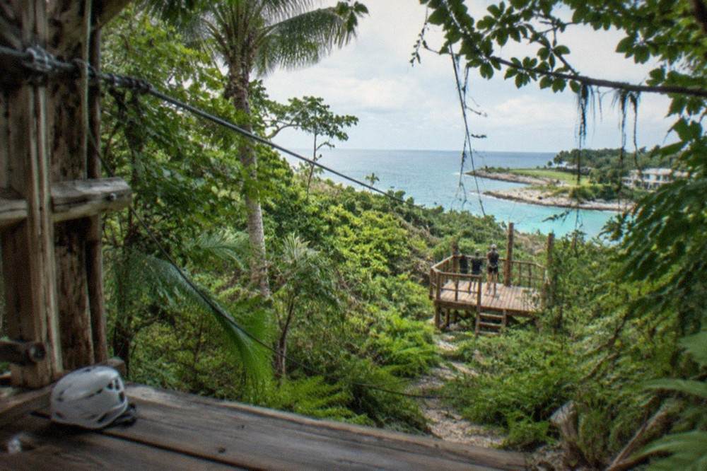A zipline cable stretching through dense tropical forest toward a wooden platform.