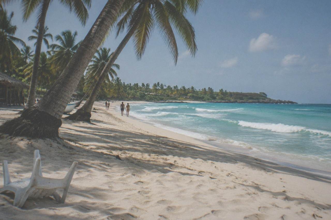 A white sand beach with leaning palm trees and clear turquoise water on a Caribbean island.