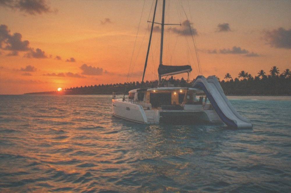 A private catamaran with a water slide extended from the side, anchored in calm blue ocean