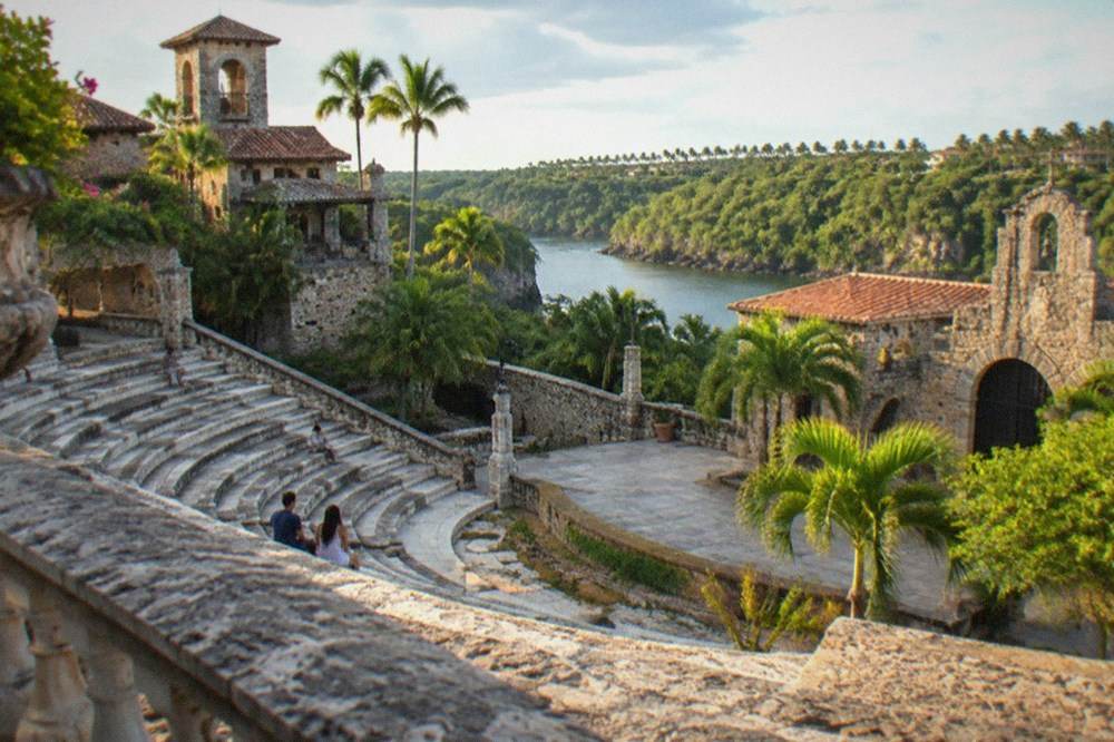 Terracotta-roofed stone amphitheater at Altos de Chavón with the Chavón River in the background under a partly cloudy sky