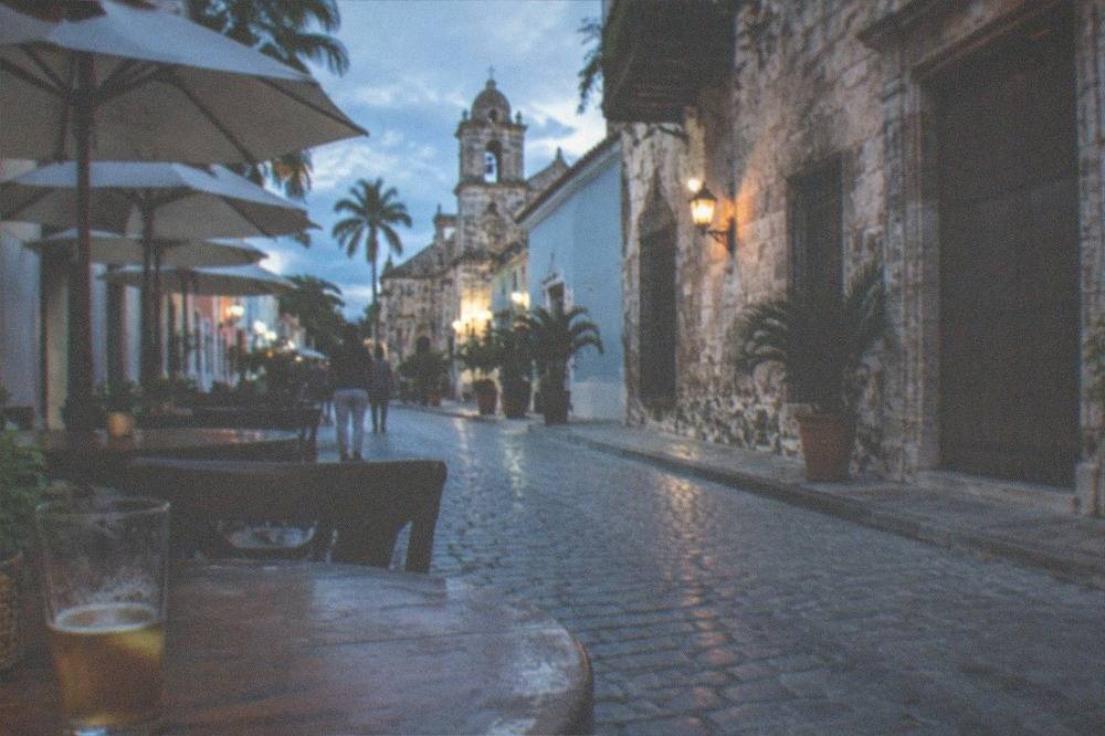 Colorful colonial buildings along a narrow cobblestone street with restaurant tables and umbrellas in Santo Domingo's Zona Colonial