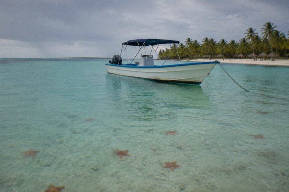 Shallow turquoise water over a sandy seabed with starfish visible near a stationary boat
