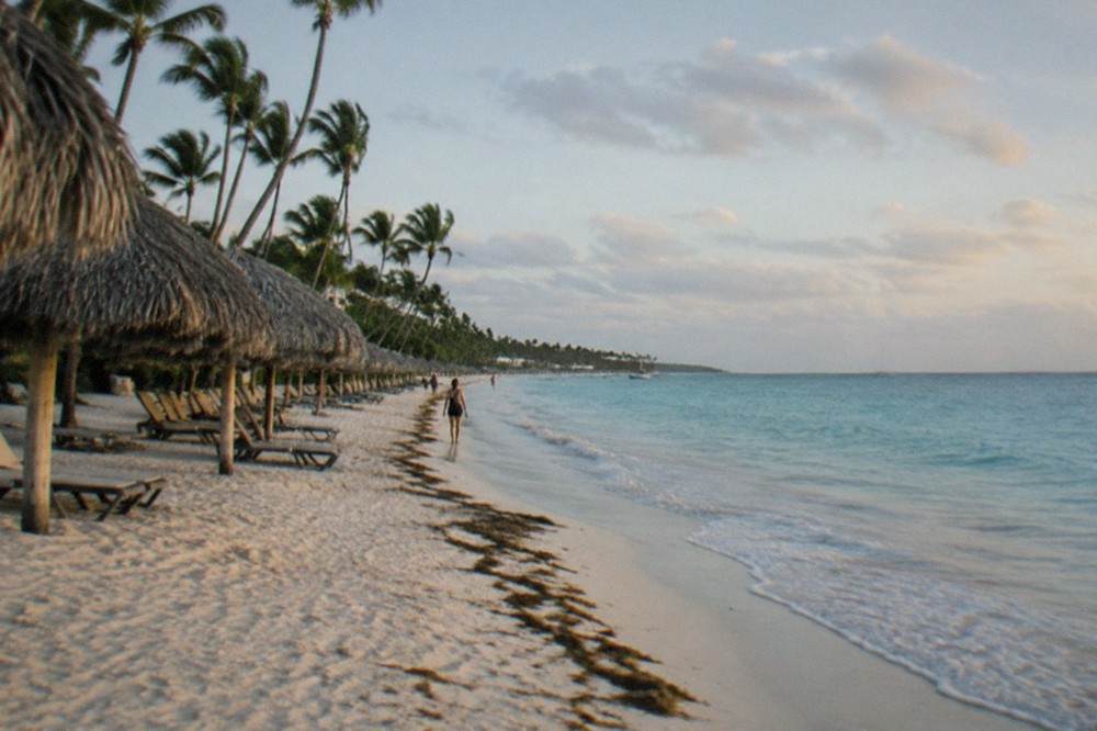 A quiet stretch of Bavaro beach with thatched umbrellas and calm turquoise water in early morning light.
