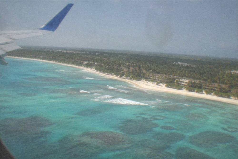 Airplane wing above turquoise Caribbean coastline seen from a window seat