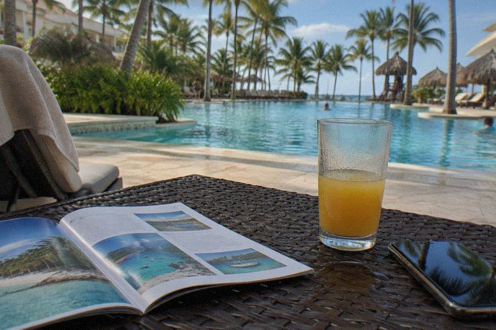 Open tour booklet and phone on a resort table beside a palm-lined pool deck