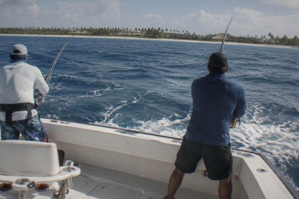 Anglers on the deck of a fishing charter with rods in holders and open ocean behind