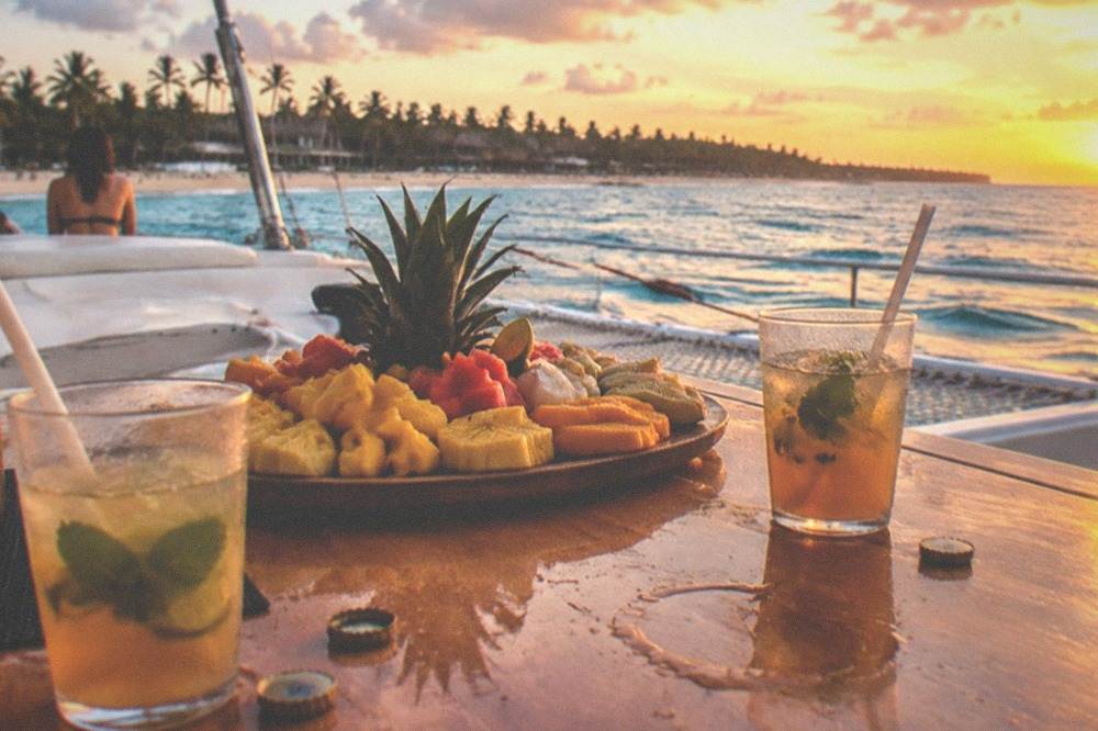 Table on a catamaran deck with a fruit platter and drinks at sunset