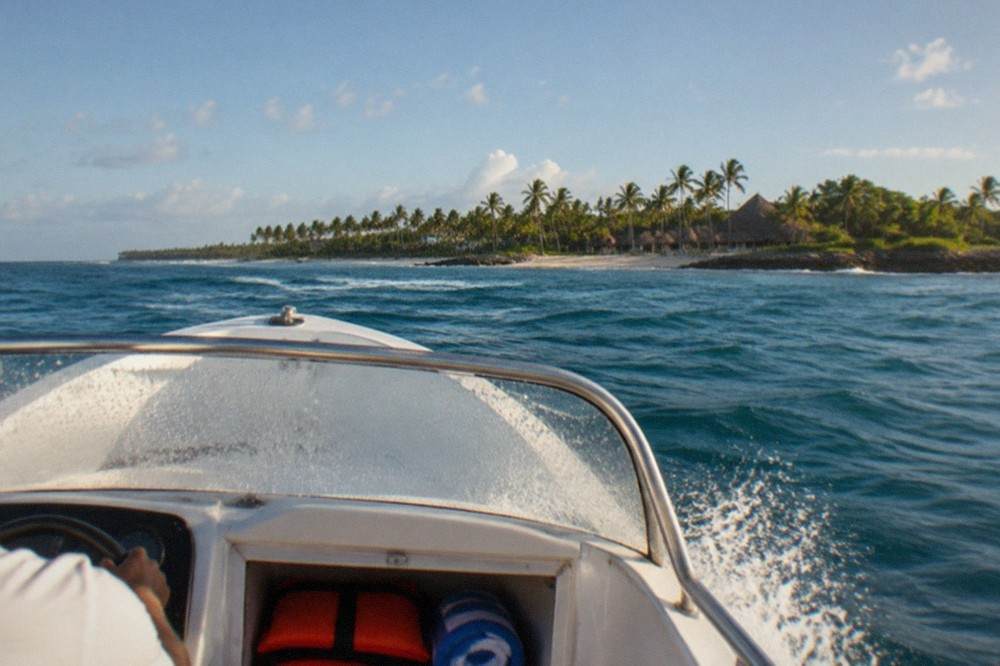 A speedboat crossing open turquoise water toward a palm-covered island
