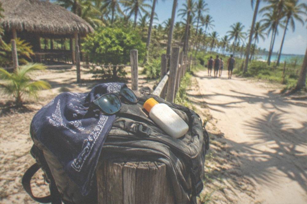 Sunglasses, a folded bandana and a sunscreen bottle resting on a backpack in bright sunlight