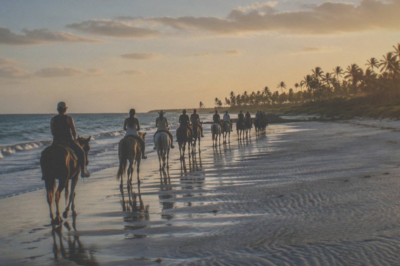 Riders on horseback along the Macao Beach shoreline, surf meeting the sand as the group moves down the coast.